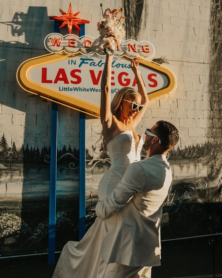 a man and woman standing in front of a las vegas sign holding up a cat