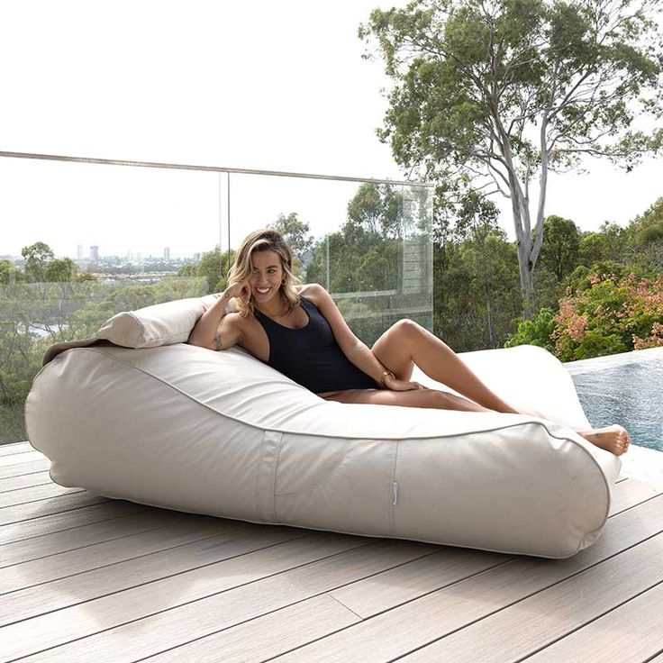 a woman laying on top of a bean bag chair next to a swimming pool with trees in the background