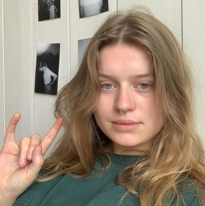 a woman making the peace sign with her hand in front of her face and photos on the wall behind her