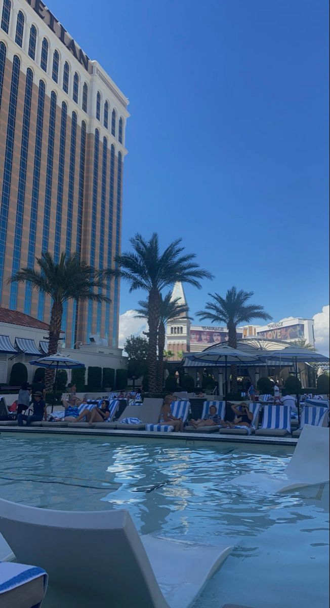 people are lounging at the edge of a swimming pool in front of a hotel