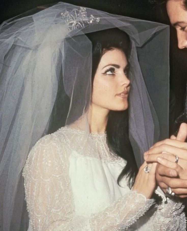 a man and woman standing next to each other in front of a white veil on their wedding day