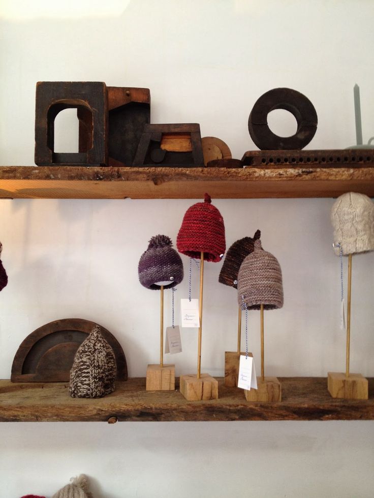 several knitted hats on wooden sticks in front of a shelf with other items behind them