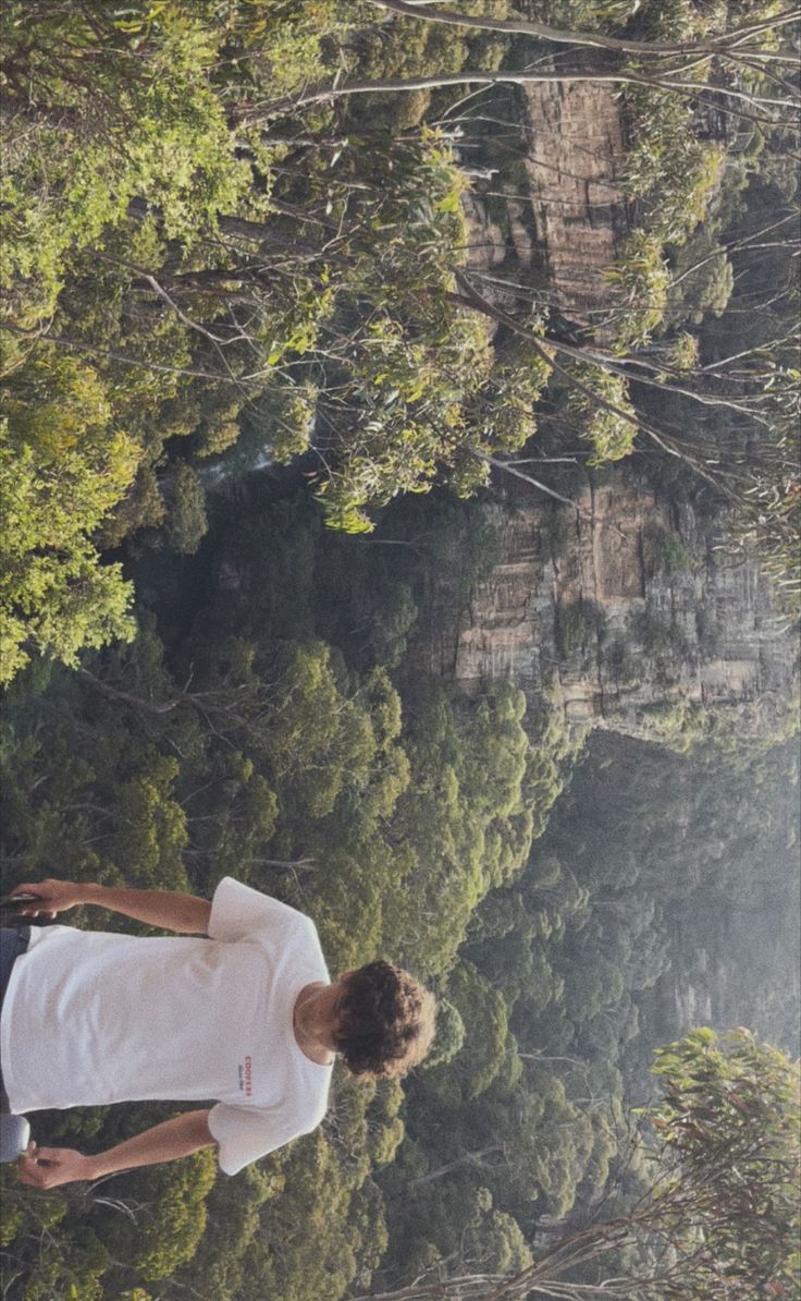 a man standing in the middle of a forest looking up into the sky with his hands on his hips