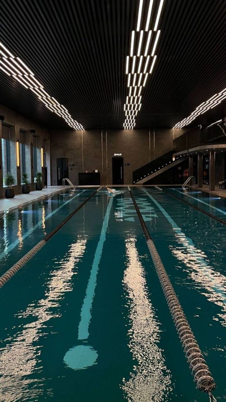 an empty swimming pool in a large building with lights on the ceiling and windows above it