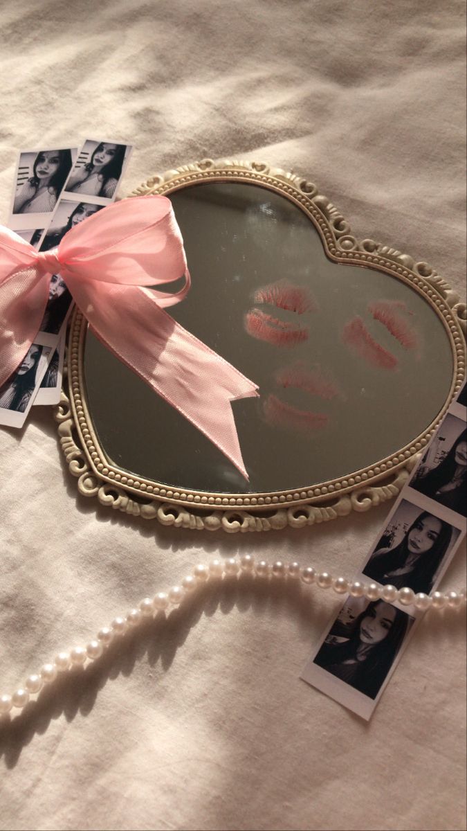 a heart shaped mirror sitting on top of a bed next to photos and a pink bow