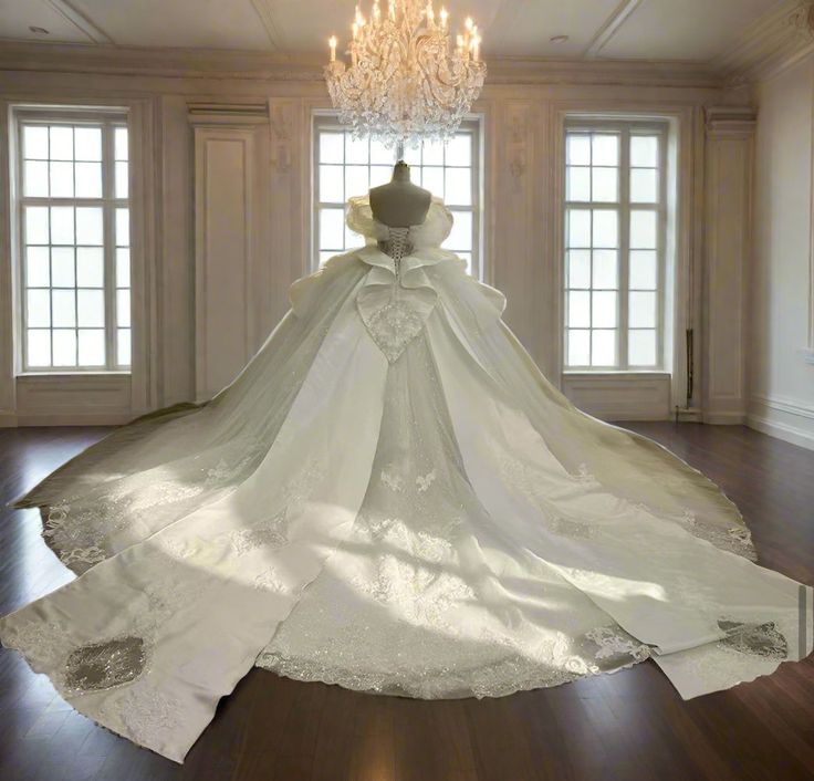 a white wedding gown is on display in a room with chandelier and windows