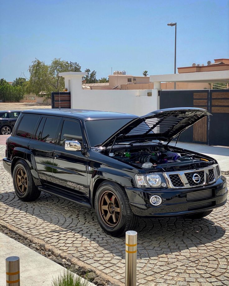 a black suv with its hood open parked in front of a building on a cobblestone driveway