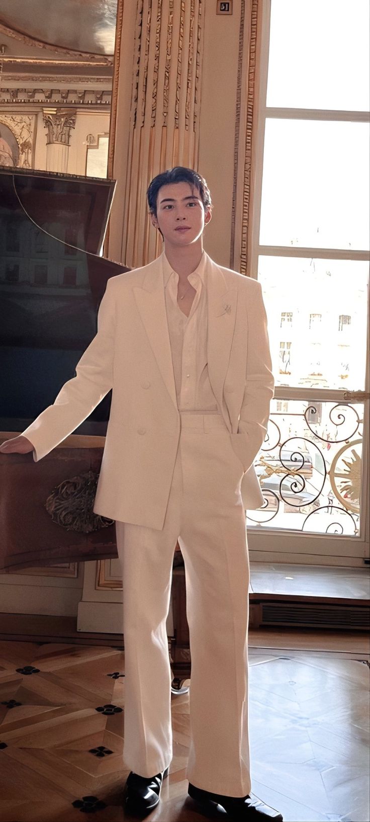 a man standing in front of a piano wearing a white suit and black shoes with his hands on his hips