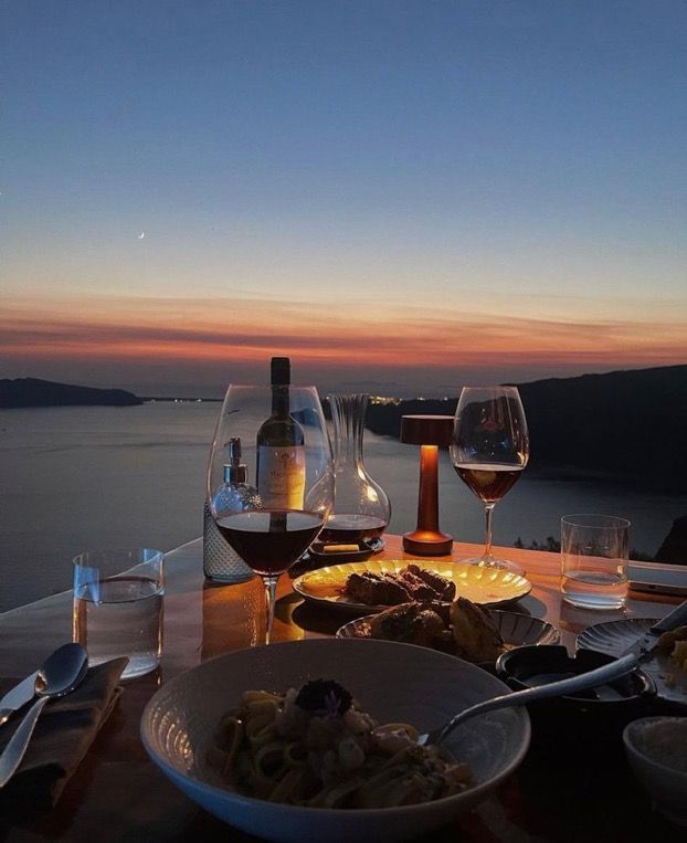 two glasses of wine are sitting on a table with food and drinks in front of the ocean