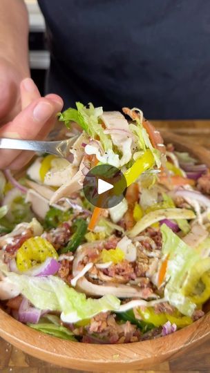 a person is cutting into a salad in a wooden bowl with a knife and fork