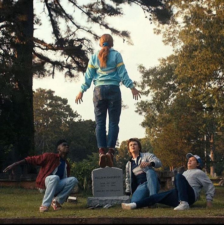 three people are sitting on the ground in front of a monument and one person is jumping up into the air