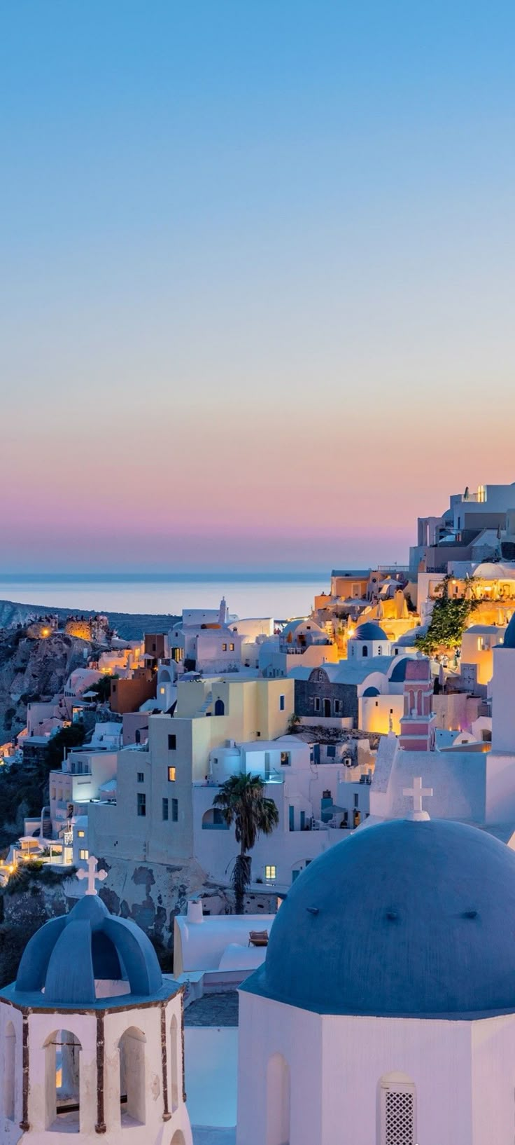 the sun is setting over some white buildings and blue domes in front of an ocean