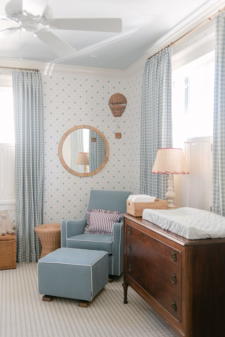 a baby's room with a blue chair, dresser and mirror on the wall