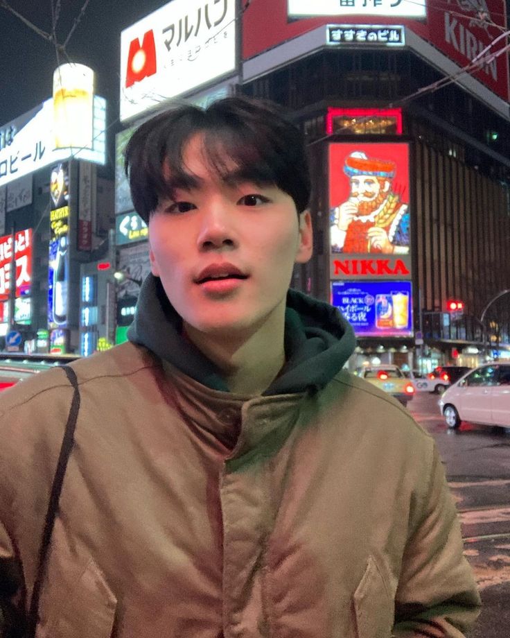 a man standing in front of a busy city street at night with neon signs on the buildings