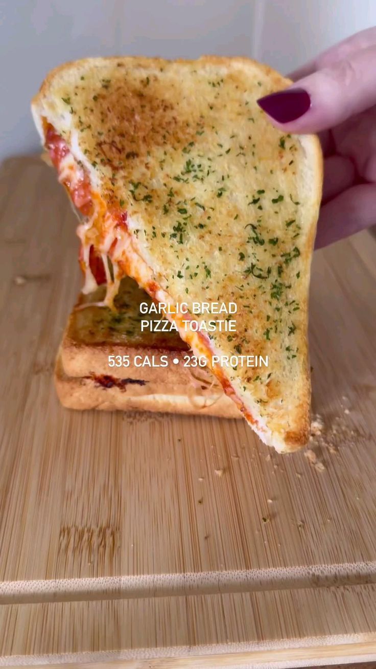 someone is holding up a piece of pizza on a cutting board that has been cut in half