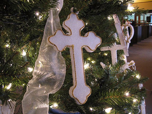 a christmas tree decorated with white and gold decorations, including a cross ornament