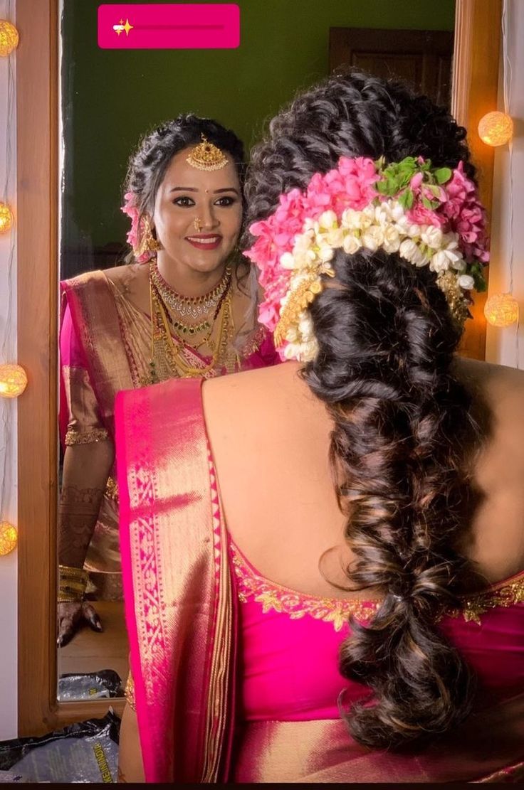 a woman in a pink sari is looking at herself in the mirror with flowers on her head