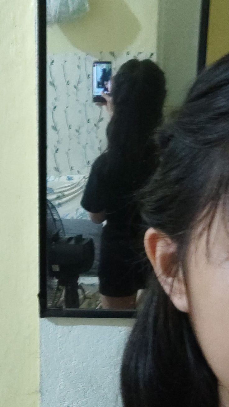 a woman taking a selfie in front of a mirror with her hair pulled back