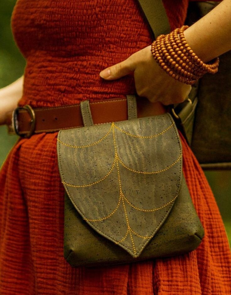 a woman in an orange dress is holding a brown leather bag with gold details on it