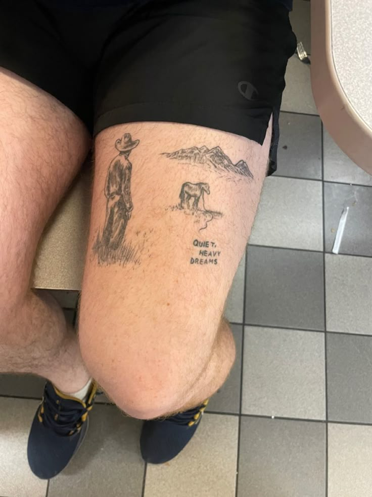 a man's legs with tattoos on them sitting on a bathroom floor next to a toilet