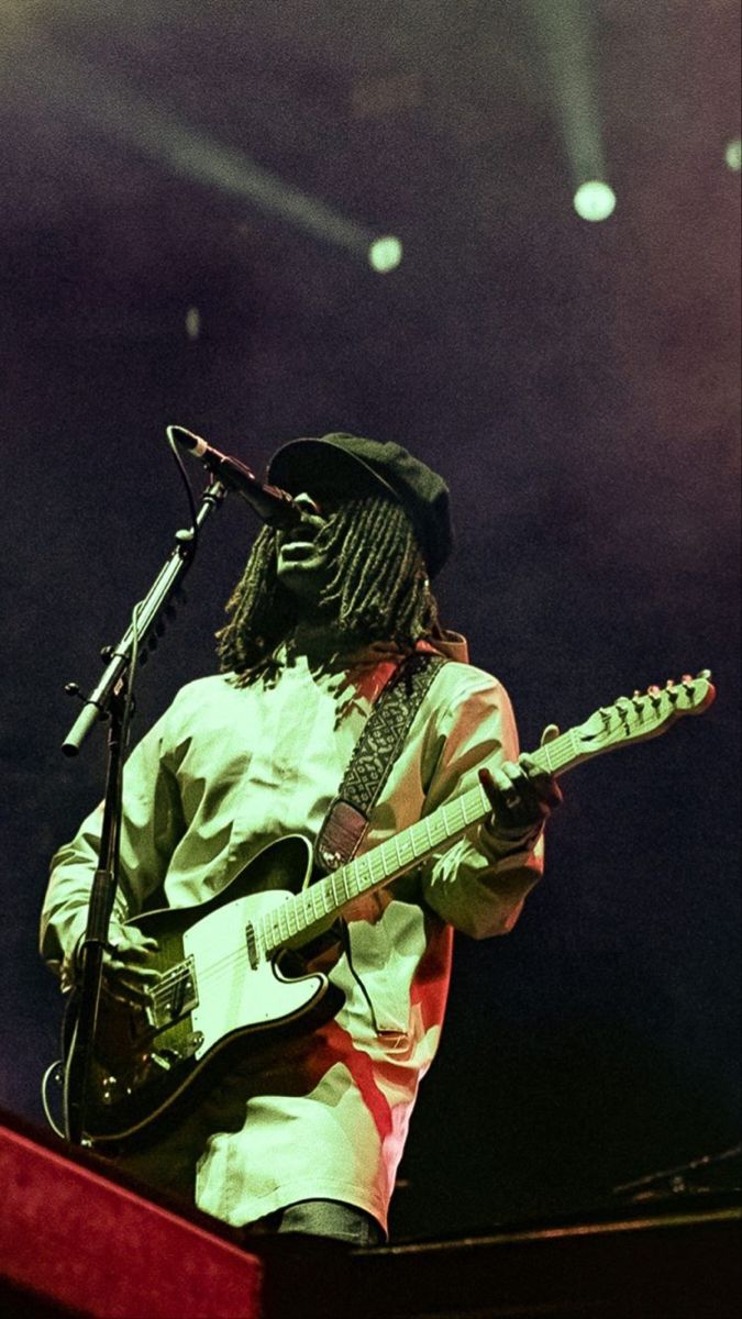 a man with dreadlocks playing an electric guitar at a music festival in front of a microphone