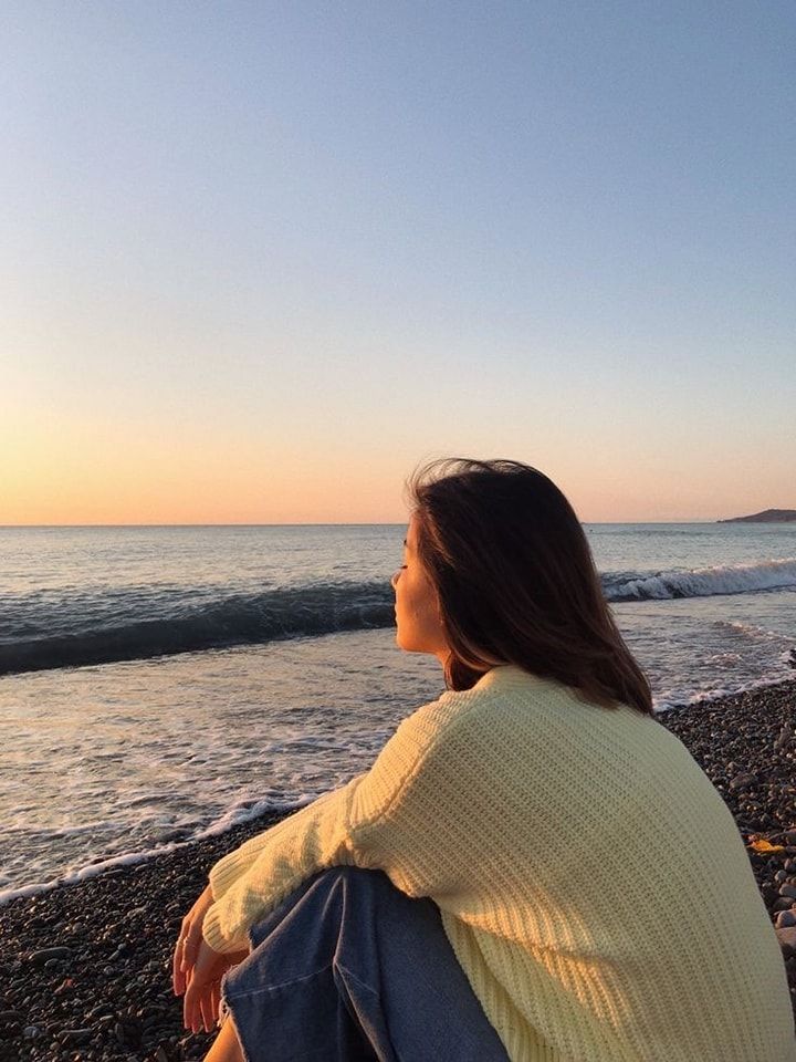 a woman sitting on top of a beach next to the ocean watching the sun go down