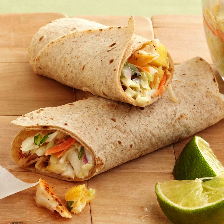 two burritos cut in half on a cutting board next to lime wedges