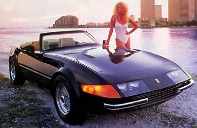 a woman standing on top of a black sports car next to the ocean with buildings in the background