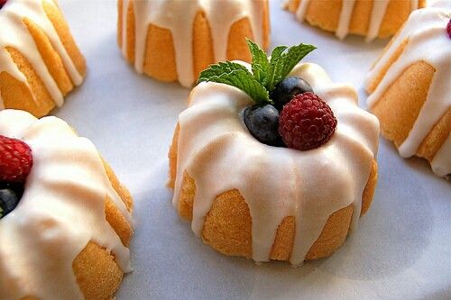 several small cakes with icing and berries on top