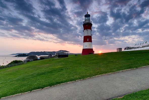 a red and white light house sitting on top of a lush green hillside next to the ocean