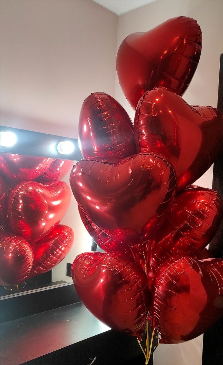 a bunch of red heart shaped balloons in front of a mirror