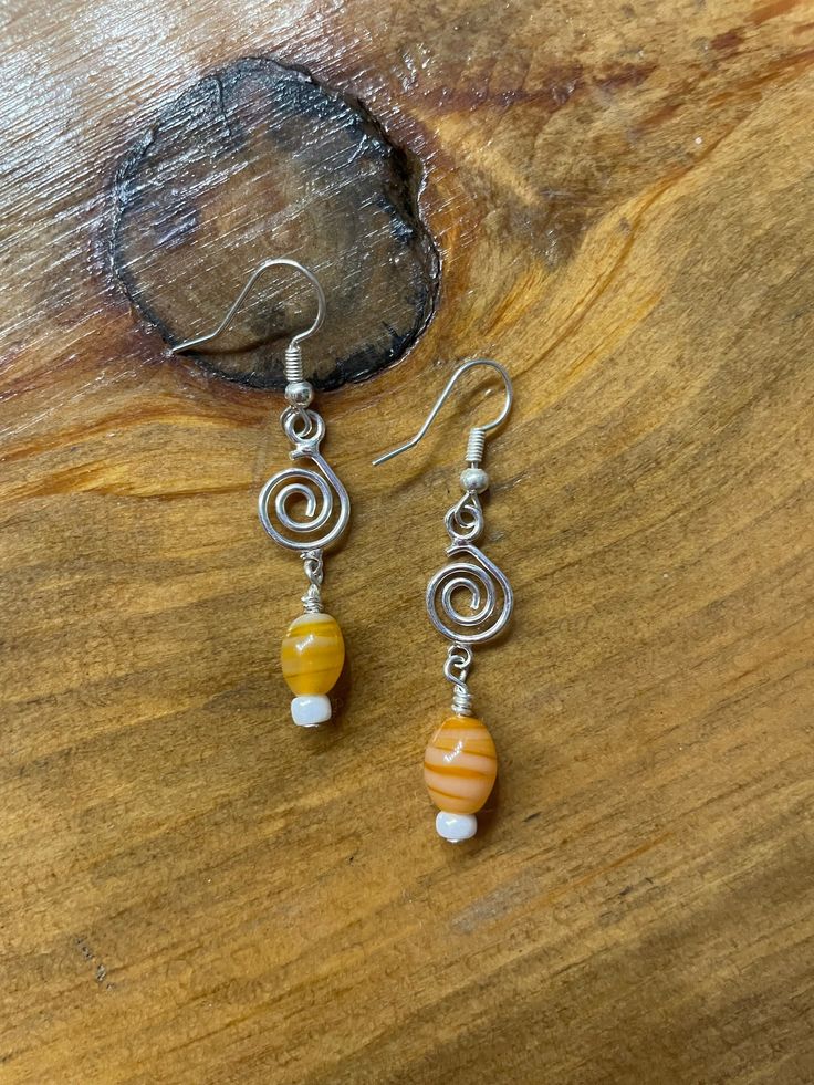 two different colored beads are hanging from silver earwires on a wooden surface with a piece of wood in the background