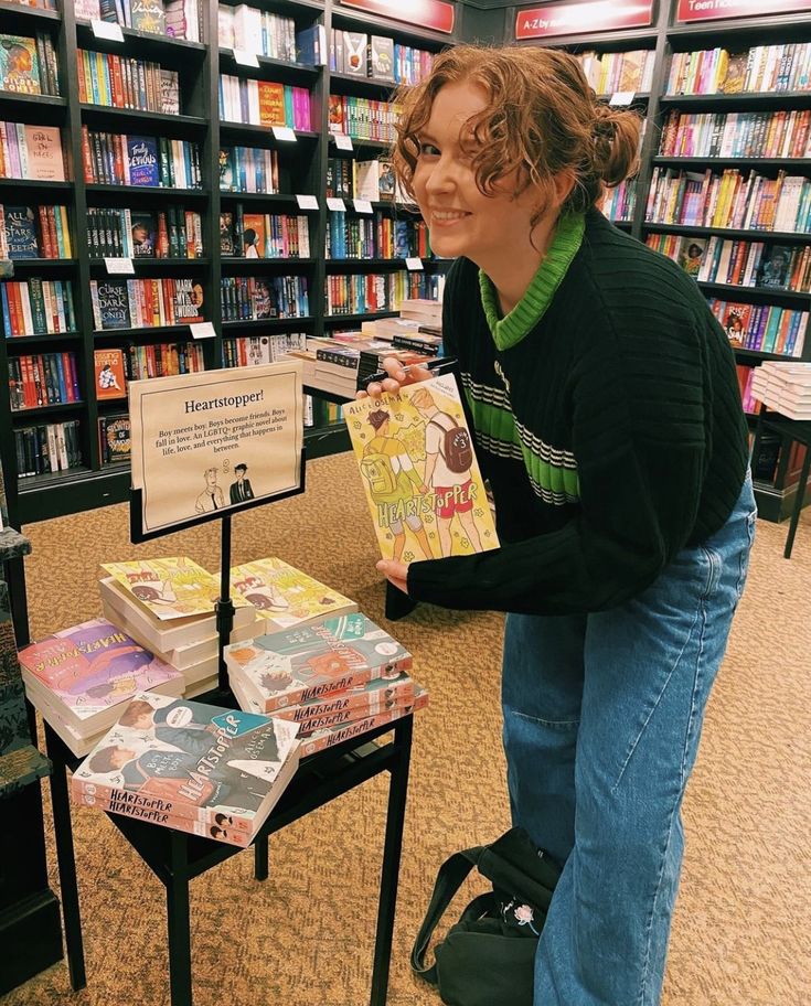 a woman standing next to a table with books on it in a library filled with lots of books