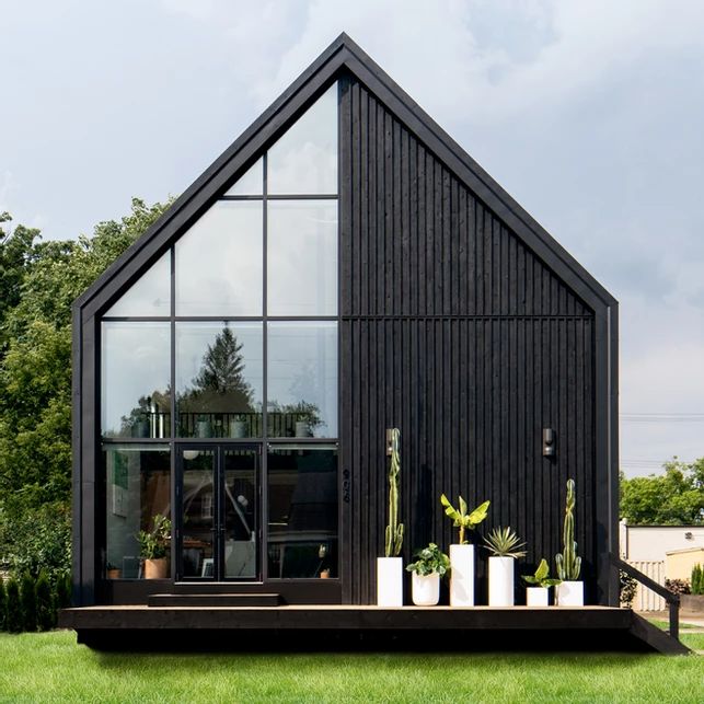 a black house with glass windows and plants on the front porch, surrounded by green grass