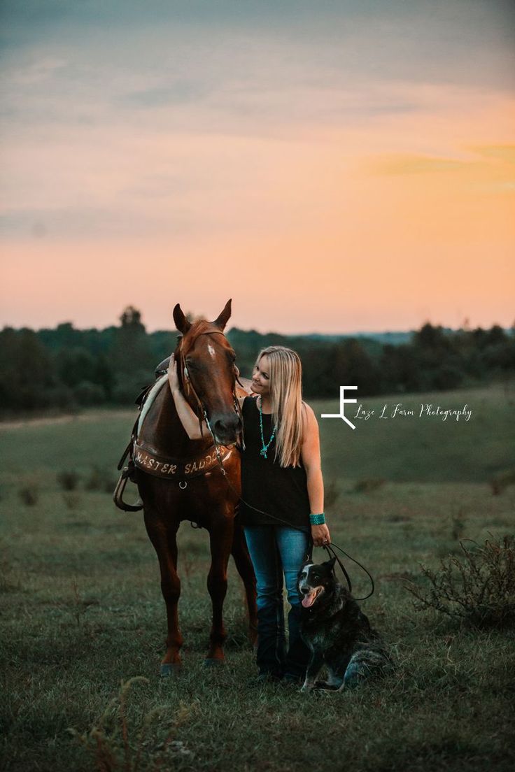 a woman standing next to a brown horse on top of a lush green field at sunset