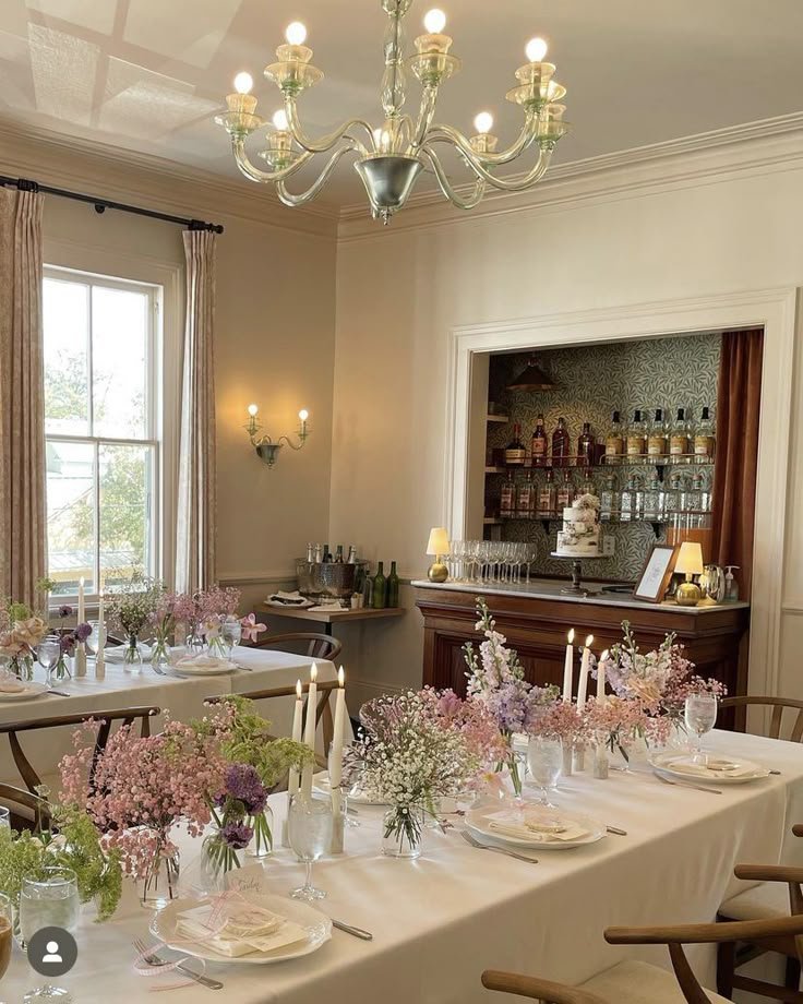 a dining room table set up with flowers and candles in front of the window for an event