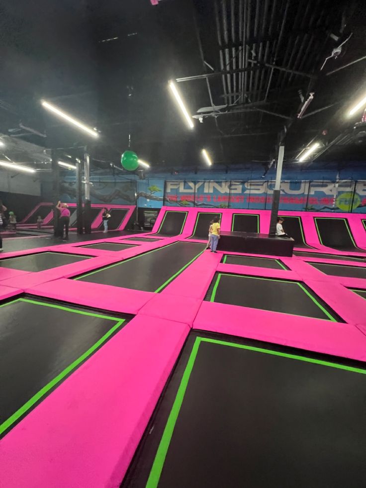 an indoor trampoline park with pink and green lines on the ground, people are standing in the background