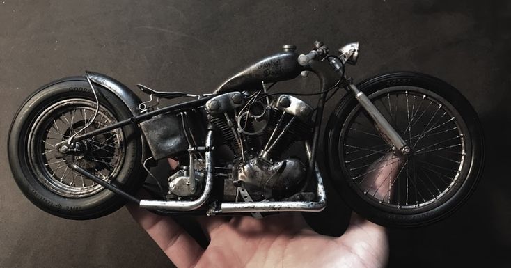 a miniature motorcycle is being held in the palm of a person's hand on a black background