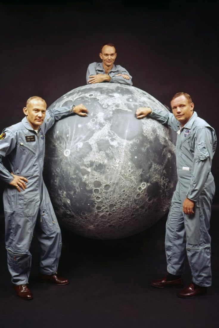 three men in space suits standing next to a large object with the moon on it