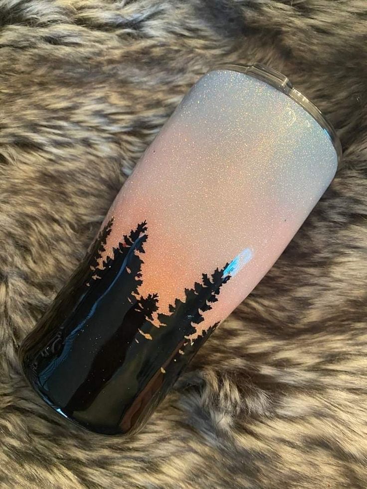 a black and white tumbler with trees on it sitting on top of a furry surface