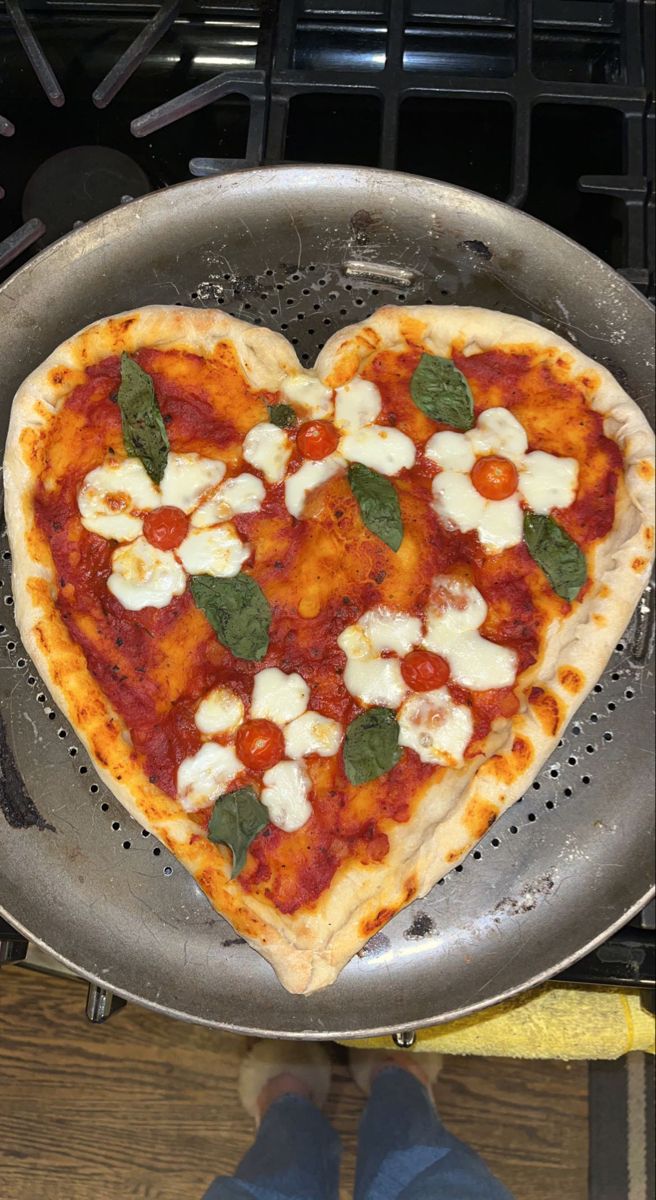 a heart shaped pizza sitting on top of a metal pan in front of a stove