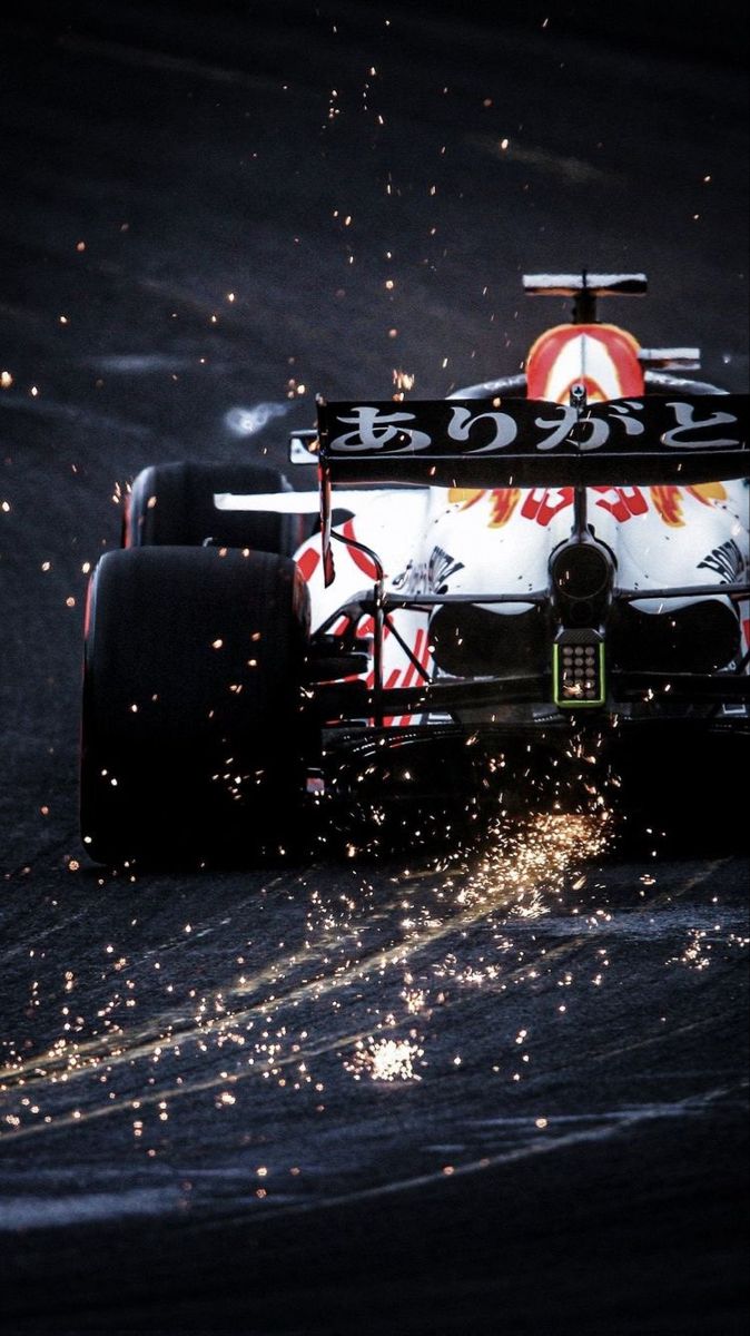 a red and white race car driving down a wet track with sparks in the air