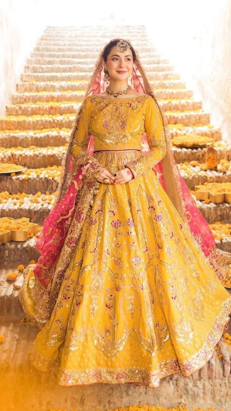 a woman in a yellow wedding dress standing on stairs with flowers all over the floor