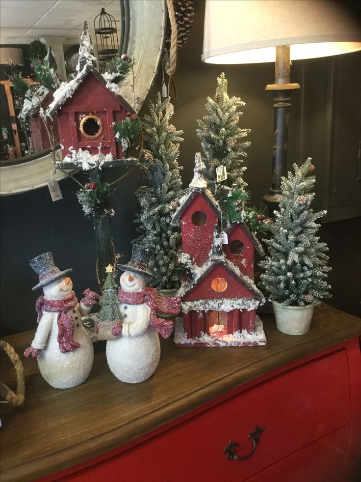 three snowmen are standing in front of christmas trees and birdhouses on a dresser