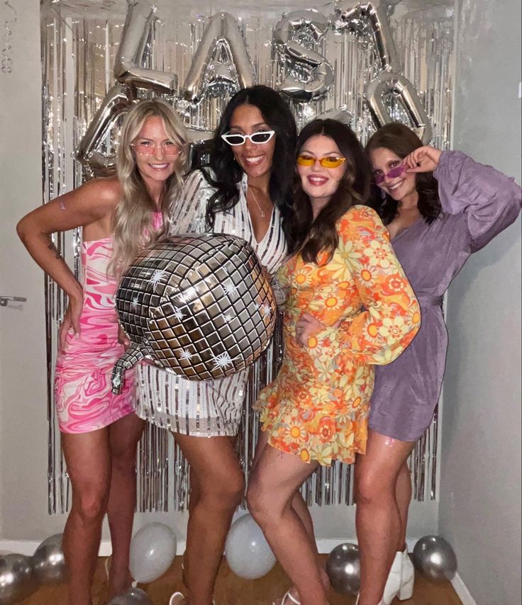 four women posing in front of a disco ball