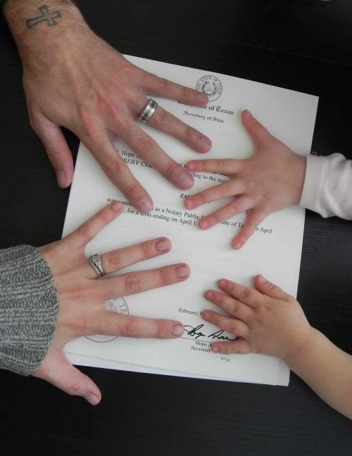 two adults and one child holding their hands over a piece of paper with writing on it