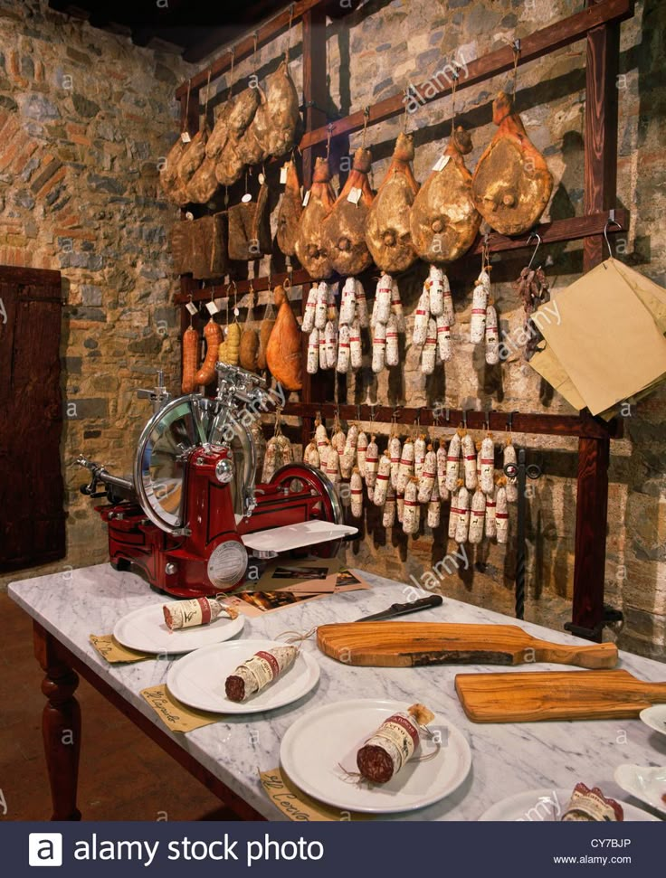 an old fashioned kitchen with meat hanging from the wall and plates on the table in front of it