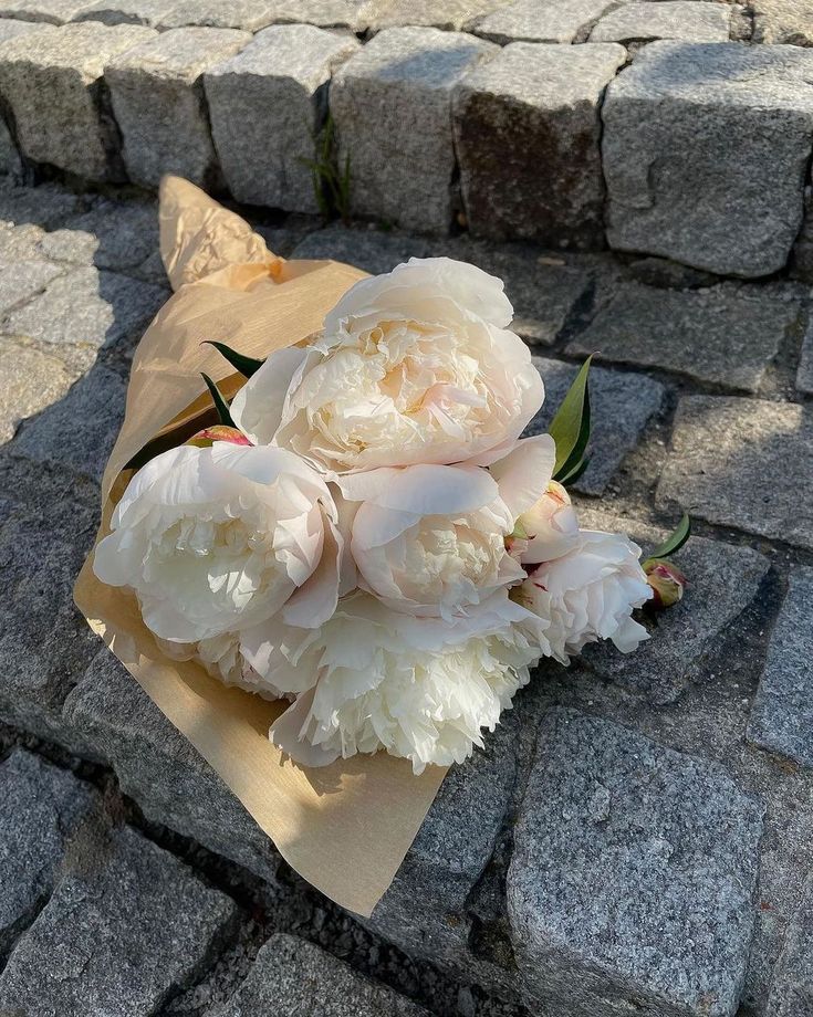 a bouquet of white peonies sitting on top of a piece of brown paper