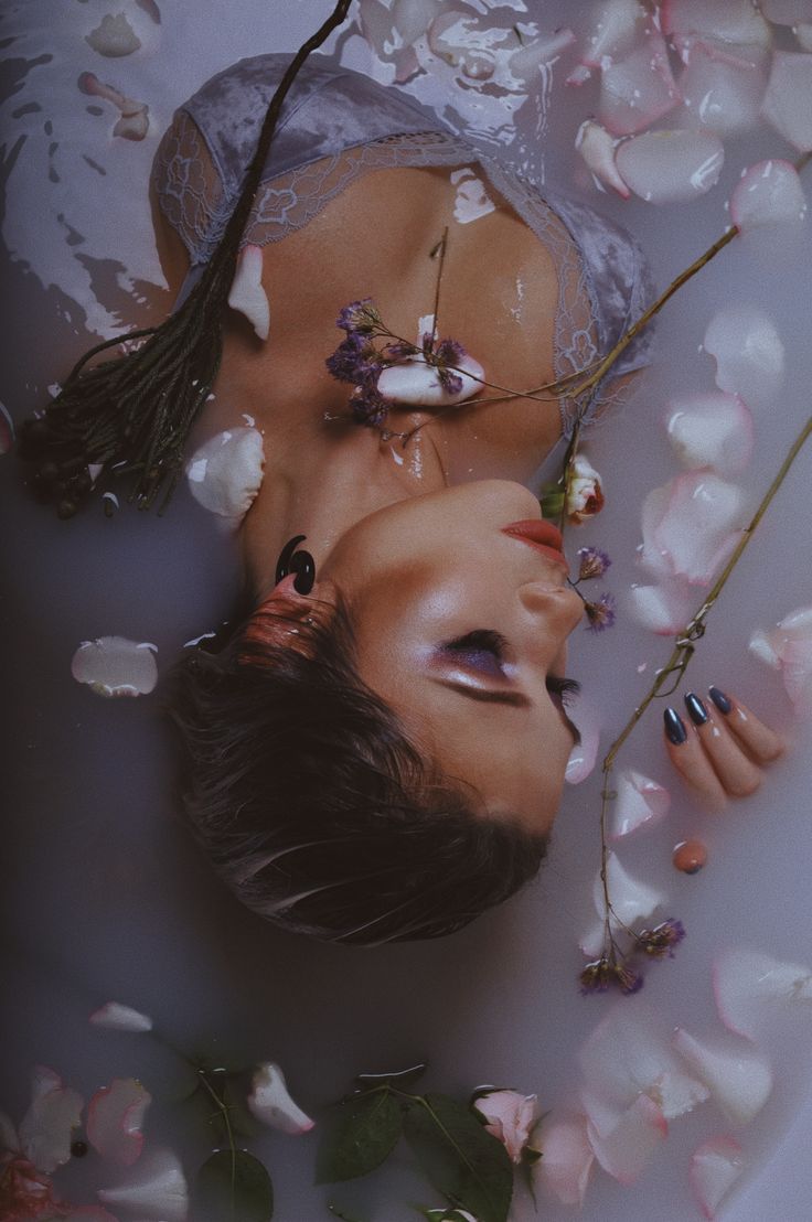 a woman laying in a bathtub with flowers all over her face and hands on the side