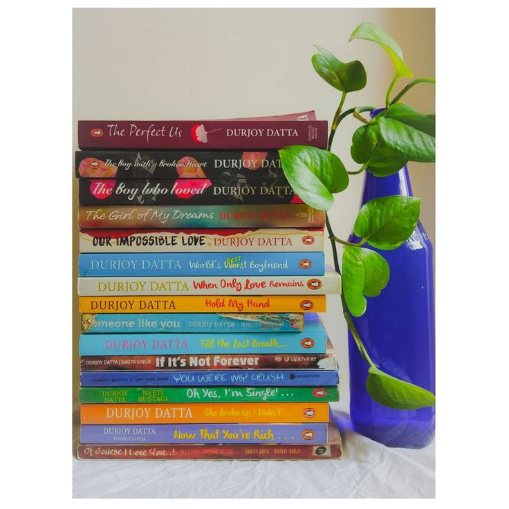 a blue vase filled with lots of books next to a stack of books on top of a table